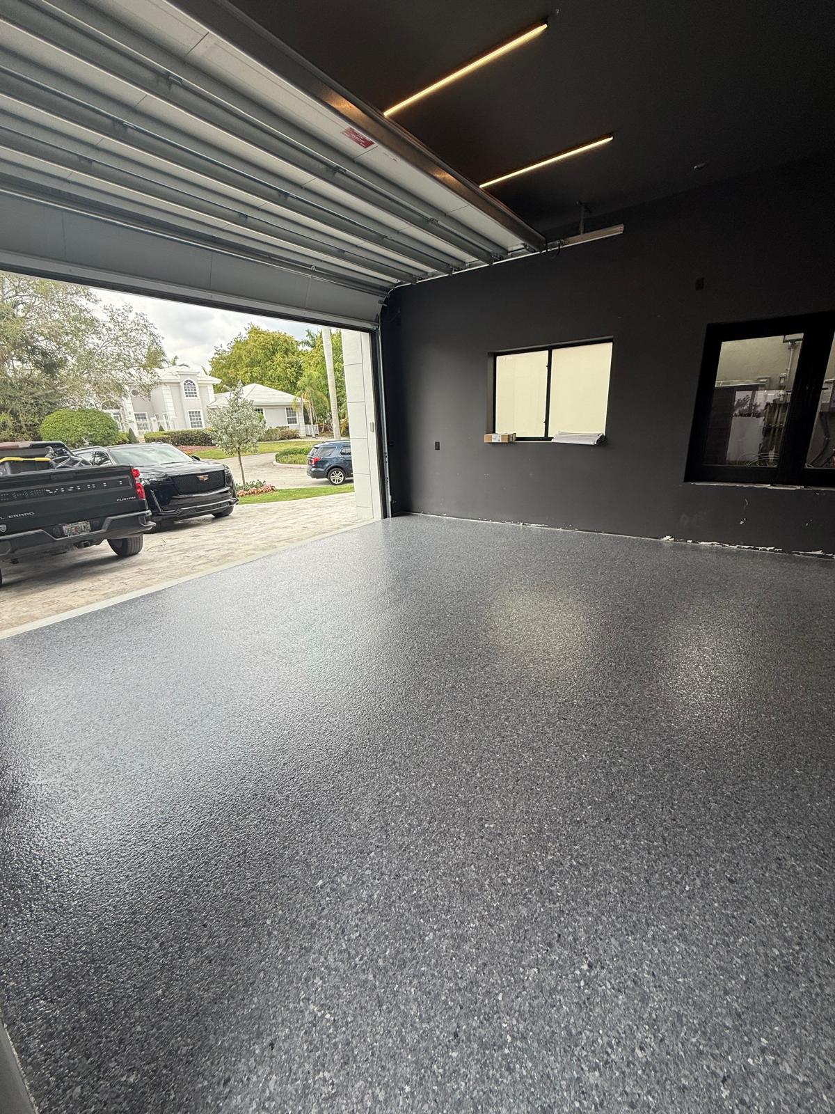Residential garage with dark gray flake epoxy floor and vehicles parked outside